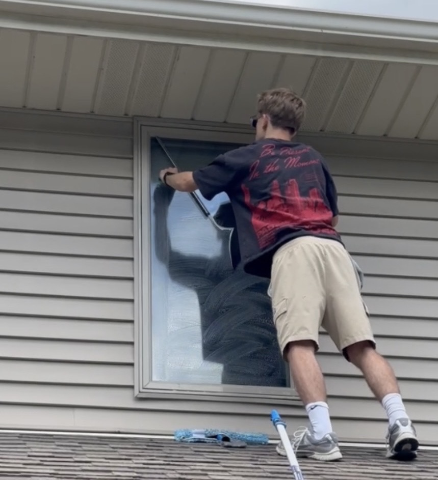 Technician cleaning a residential window from the roof with a squeegee