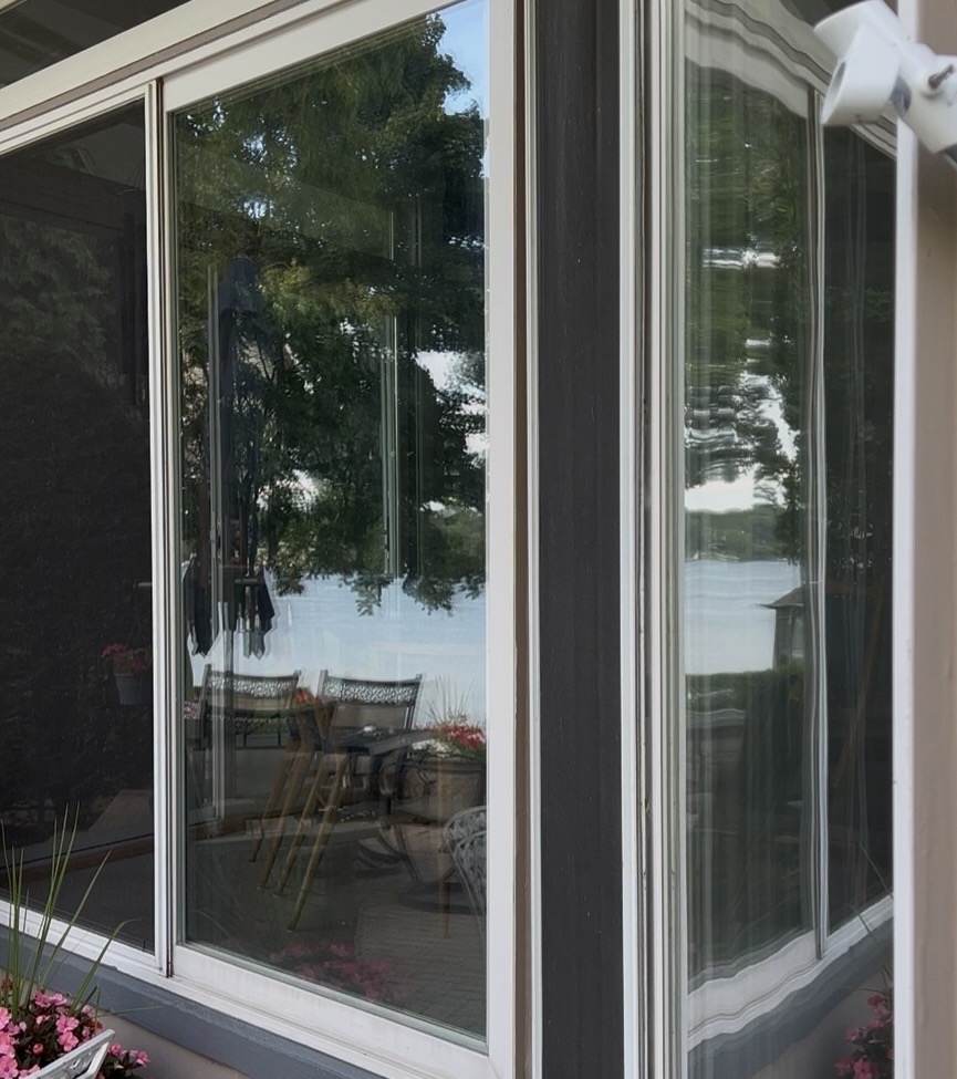 Sliding glass doors reflecting a serene lake view and patio furniture